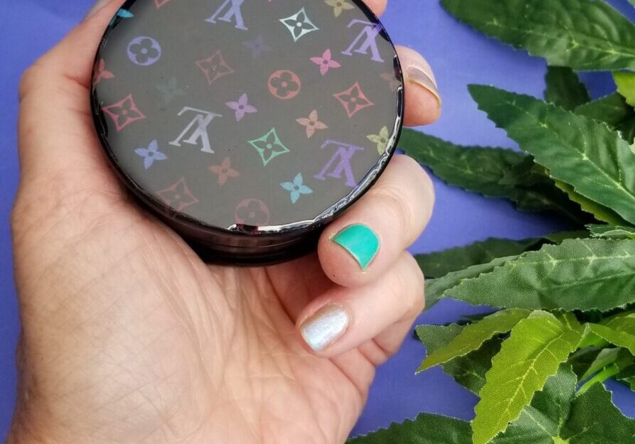 Hand holding patterned compact on purple background